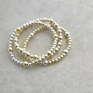 May include: Three stacked bracelets made of small gold and silver beads.