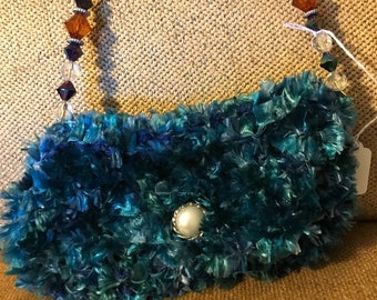 Blue Knitted handbag with a multicolored jeweled handle. Button closure. Sparkly silver insides.