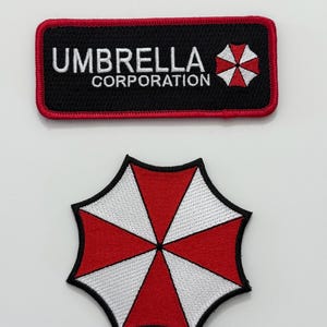 May include: Two embroidered patches. The top patch reads "UMBRELLA CORPORATION" in white on a black background, with a red border and an umbrella logo. The bottom patch is an umbrella logo in red and white, with a black outline.
