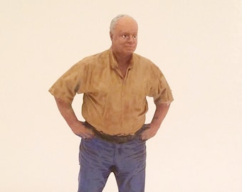 May include: A figurine of a man wearing a tan short-sleeved shirt and blue jeans. He is standing with his hands on his hips.