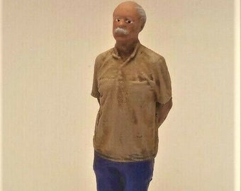 May include: A figurine of a man wearing a brown shirt and blue jeans. He has white hair and a mustache.