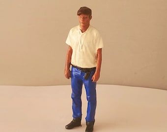 May include: A miniature plastic figurine of a person wearing a white shirt, blue jeans, and a brown cap.