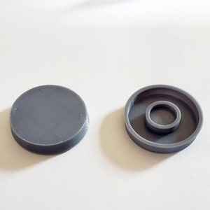 May include: Two gray plastic caps, one with a flat top and the other with a recessed center. The caps are designed to cover screw holes.