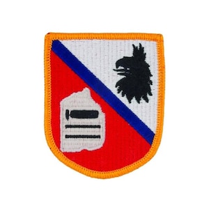 Op de afbeelding: Een geborduurde patch in rood, wit en blauw met een zwarte adelaar en een wit gebouw met een zwarte deur en ramen. De patch is omgeven door een gele rand.