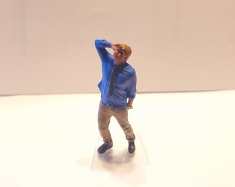 May include: A miniature figurine of a person wearing a blue shirt and khaki pants. The person is holding their hand to their forehead as if looking into the distance.