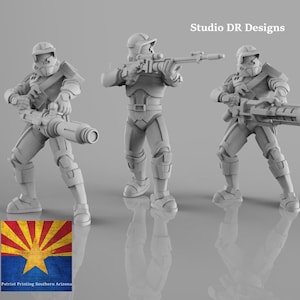 Puede incluir: Tres figuras de color gris claro con armadura futurista, cada una sosteniendo un arma. Las figuras están de pie en fila, una de ellas sosteniendo un arma cilíndrica grande. La imagen incluye el texto "Studio DR Designs" y un logo con el texto "Patriot Printing Southern Arizona."