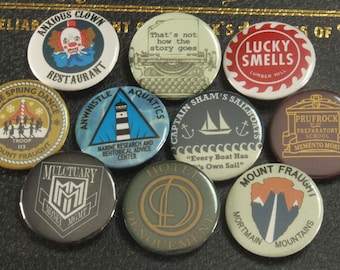 May include: Nine colorful round buttons with various designs and text. The buttons feature a clown, a lighthouse, a sailboat, a typewriter, a mountain range, a building, a hotel, a money management logo, and a dancing group.