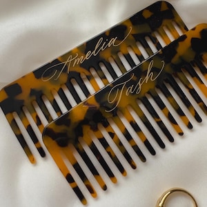 Könnte beinhalten: Zwei Schildpattkämme mit den Namen "Amelia" und "Tash", die in goldenen Buchstaben graviert sind.