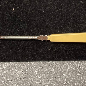 Peut inclure: Un chausse-pied vintage avec un crochet en métal et une poignée en plastique crème.