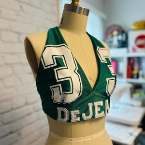 May include: Green and white halter top with the number "3" and the name "DEJEA" on the front.