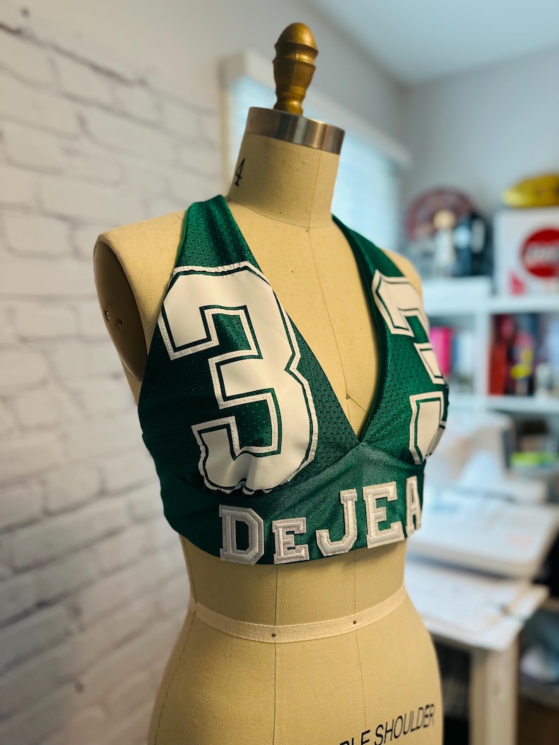 May include: Green and white halter top with the number "3" and the name "DEJEA" on the front.