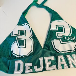 May include: Green halter top with white mesh and white numbers "32" and the name "DEJEAN" in white. The top has a white "EAGLE" patch on the right side.