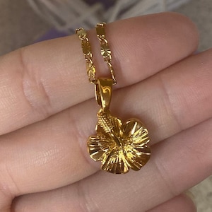 May include: A gold chain necklace with a gold hibiscus flower pendant.