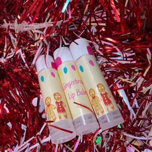 May include: Three white tubes of gingerbread lip balm with a gingerbread couple design and the text "Gingerbread Lip Balm".