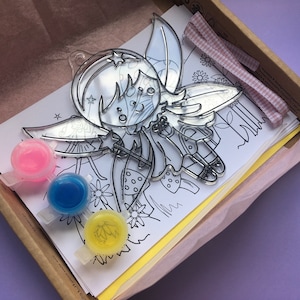 Può includere: Un kit per l'artigianato che comprende un contorno di fata in plastica trasparente con ali, un pennello e tre piccoli flaconi di vernice rosa, blu e gialla. Il kit include anche un foglio di carta con un disegno di fata da colorare.