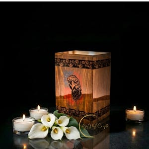 Könnte beinhalten: Eine Holzkiste mit einem Adlerdesign, umgeben von brennenden Kerzen und weißen Calla-Lilien. Die Kiste hat eine rechteckige Form mit einem geschnitzten Blumenmuster oben und einer Adlerillustration auf der Vorderseite. Der Hintergrund ist schwarz.