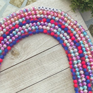 May include: A set of colorful beaded necklaces with the names "HANNAH" and "HOPE" spelled out in white letters. The beads are a mix of iridescent and solid colors, including pink, blue, and red.