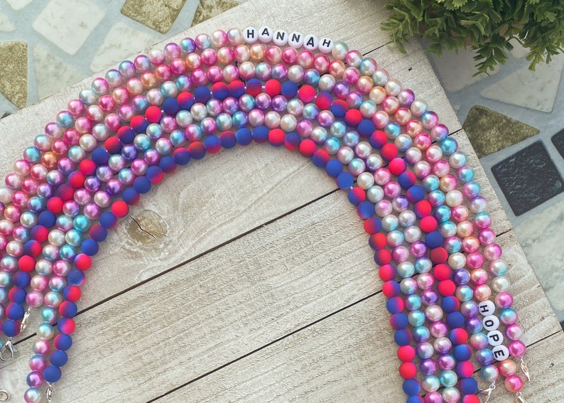 May include: A set of colorful beaded necklaces with the names "HANNAH" and "HOPE" spelled out in white letters. The beads are a mix of iridescent and solid colors, including pink, blue, and red.
