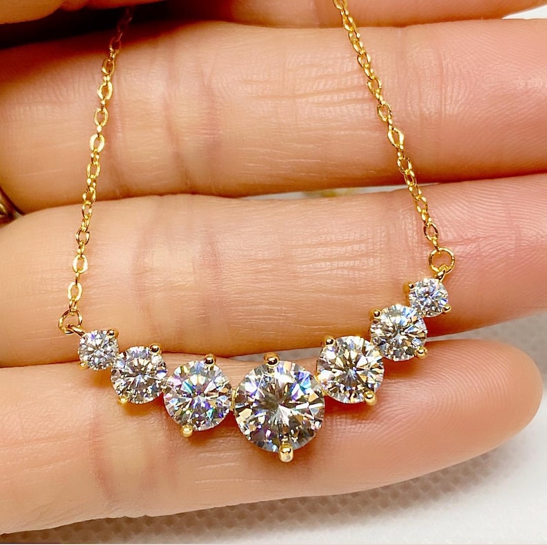 May include: A gold chain necklace with a curved row of five round, clear, sparkling stones.
