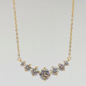 May include: A gold chain necklace with a curved row of six clear round stones.