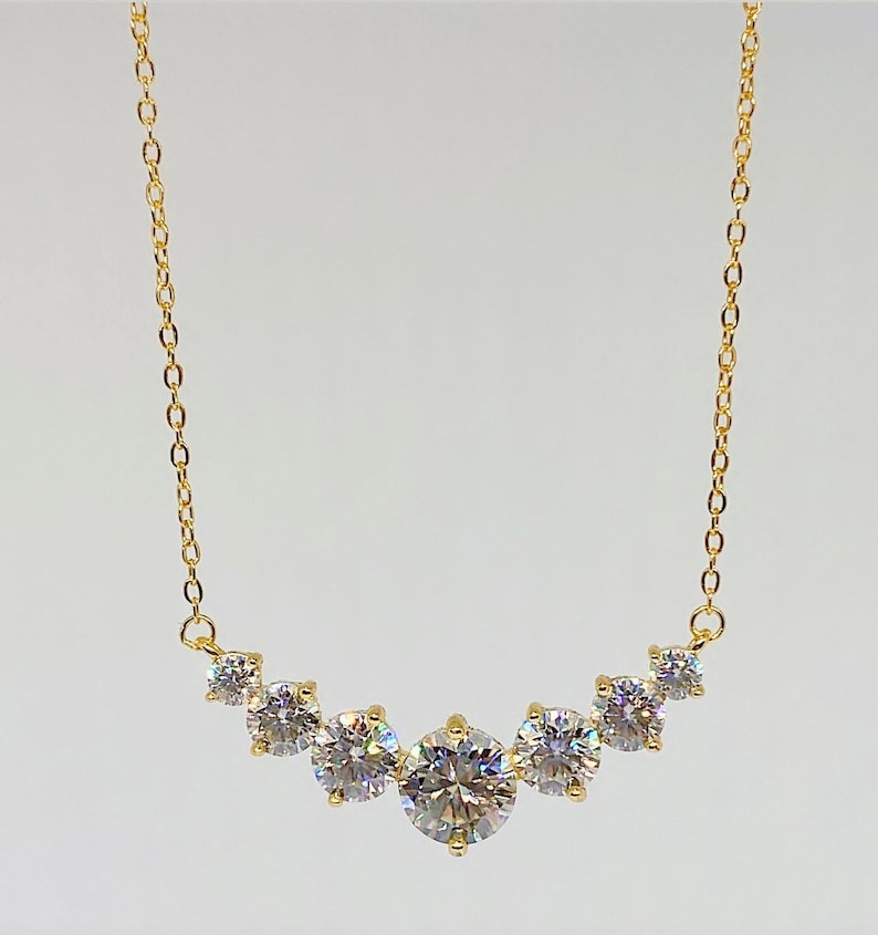 May include: A gold chain necklace with a curved row of six clear round stones.