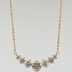 May include: A gold chain necklace with a curved row of five round, clear cubic zirconia stones.