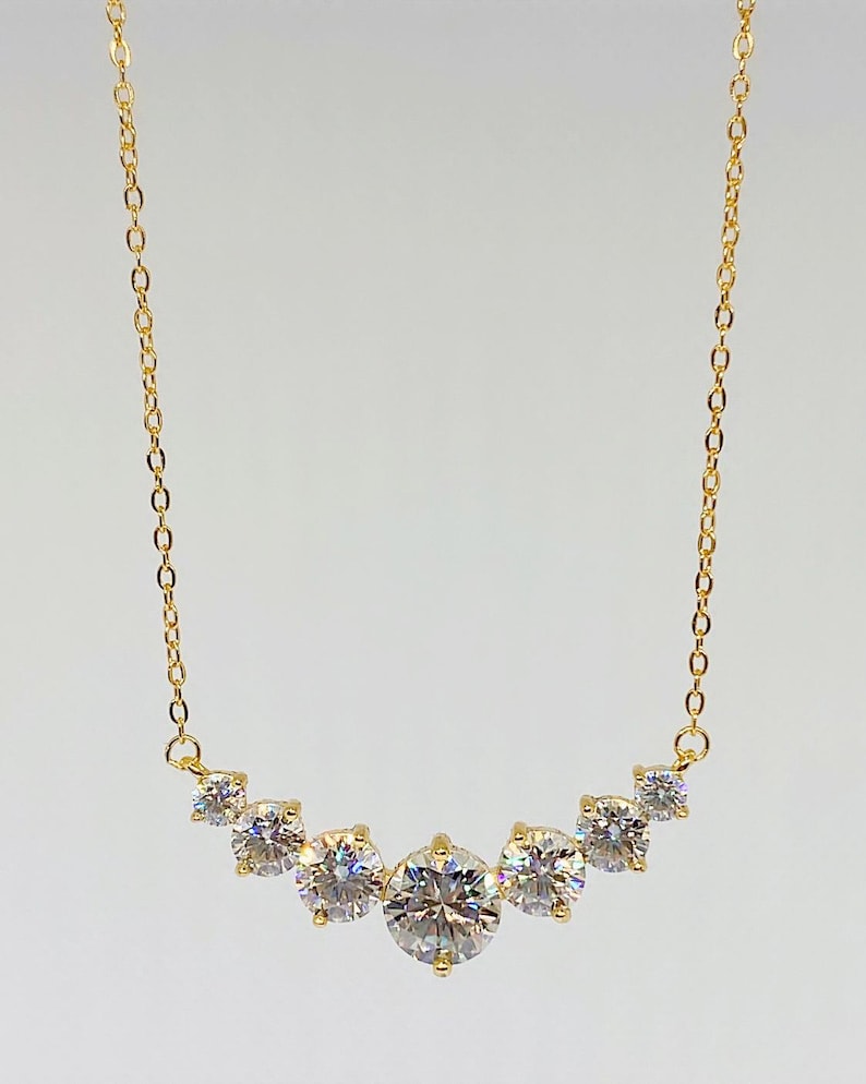 May include: A gold chain necklace with a curved row of five round, clear cubic zirconia stones.