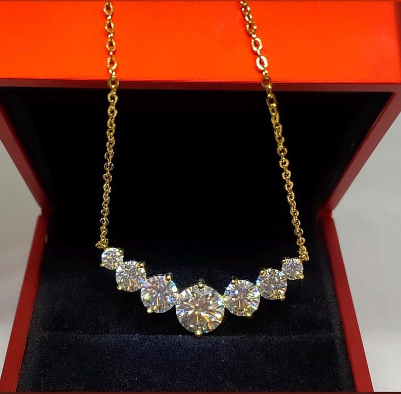 May include: A gold chain necklace with a row of six round, clear, sparkling stones. The necklace is in a red velvet box.