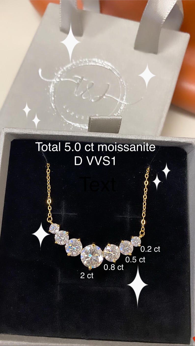 May include: A gold chain necklace with a row of five round, clear moissanite stones. The stones are labeled with their carat weight: 2 ct, 0.8 ct, 0.5 ct, and 0.2 ct. The necklace is in a black velvet box with the text "Total 5.0 ct moissanite D VVS1" on the lid.