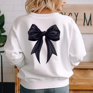May include: White sweatshirt with a large black bow printed on the back.