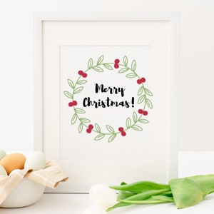 K&ouml;nnte beinhalten: Ein wei&szlig;er gerahmter Druck mit einem gr&uuml;nen Kranz mit roten Beeren und dem Text "Merry Christmas!" in Schwarz.