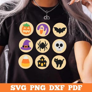 Può includere: Una t-shirt nera con una griglia di nove icone circolari con immagini di Halloween, tra cui una zucca, un fantasma, un pipistrello, un cappello da strega, un ragno, un teschio, caramelle, una casa stregata e un gatto nero.