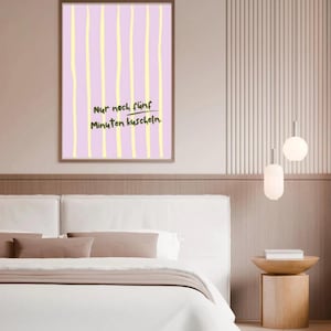 Op de afbeelding: Een ingelijste print met een lichtpaarse achtergrond en gele verticale strepen. De print bevat de Duitse tekst "Nur noch fünf Minuten kuscheln." De print wordt weergegeven boven een wit bed met een bruin hoofdbord.