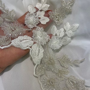 May include: Ivory floral lace applique with intricate beaded details. The design features embroidered flowers and leaves, creating a delicate and elegant pattern. Perfect for bridal wear or embellishments.