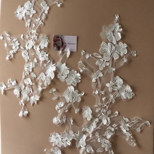 May include: Two white floral lace appliques with intricate embroidered details. The appliques feature a delicate arrangement of flowers and leaves, perfect for embellishing bridal wear or other craft projects.