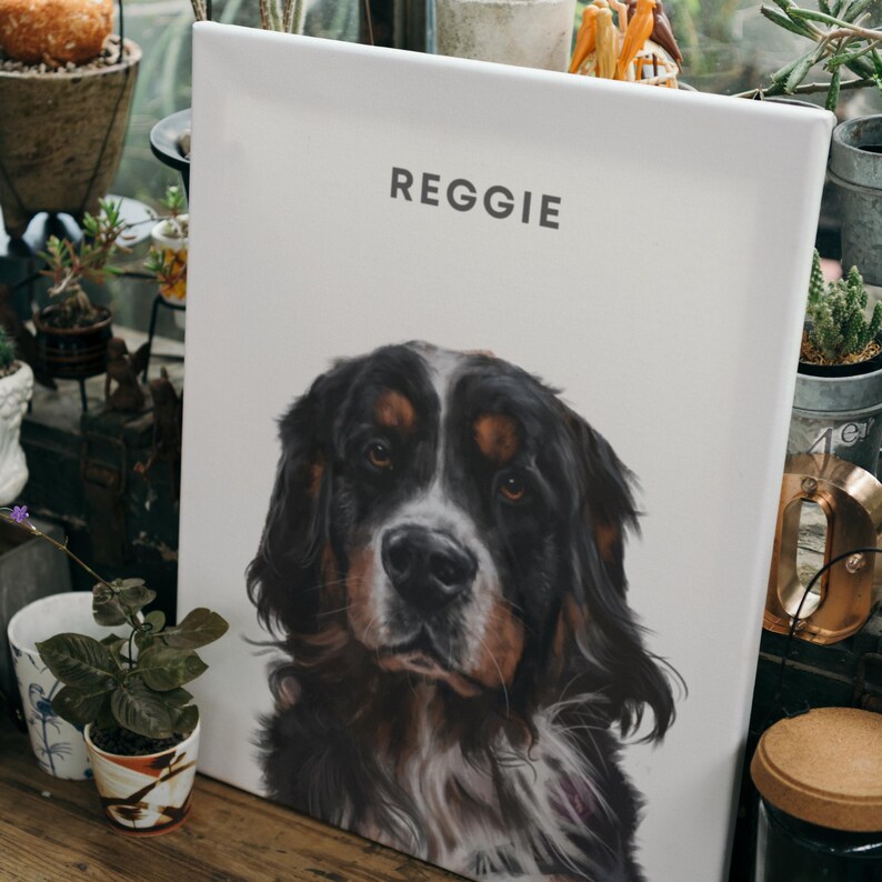 May include: A white canvas print with the name "Reggie" printed at the top. A black and brown dog with white markings is featured on the print. The dog is looking directly at the viewer.