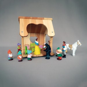 Op de afbeelding: Een houten speelhuisje met een hartvormige uitsparing, inclusief een set handbeschilderde figuurtjes waaronder een vrouw in een gele jurk, een man in een tuniek, een wit paard en diverse kleine bebaarde figuren met kleurrijke mutsen.