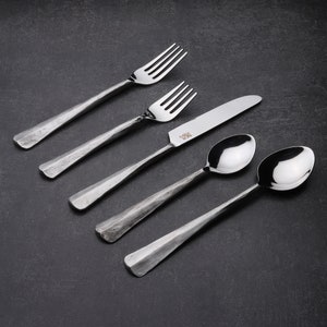 May include: A set of four silver-toned cutlery pieces, including two forks, a knife, and a spoon. The cutlery has a hammered finish and a slightly rustic look.