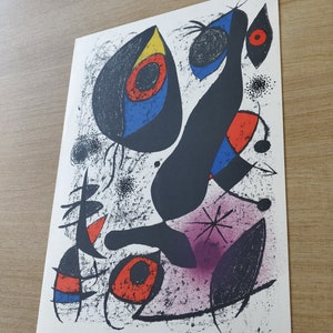 May include: Abstract art print featuring a black figure with red, blue, and yellow shapes. The background is white with black speckles and a purple area. The print is signed "Mir&oacute;" in the bottom right corner.