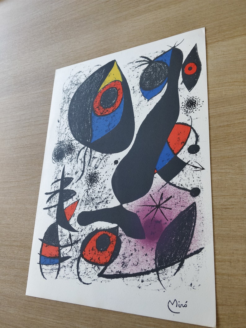 May include: Abstract art print featuring a black figure with red, blue, and yellow shapes. The background is white with black speckles and a purple area. The print is signed "Mir&oacute;" in the bottom right corner.