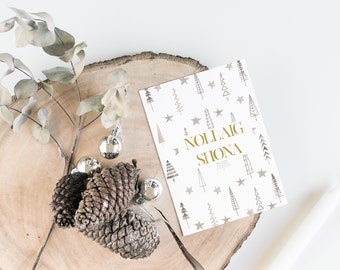 Può includere: Un biglietto bianco con un motivo dorato di alberi di Natale stilizzati e stelle. Il biglietto dice "Nollaig Shona" in lettere dorate.