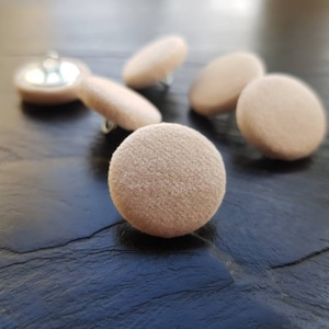 May include: A close-up of beige felt furniture protectors. The protectors are round and have a smooth, velvety texture.