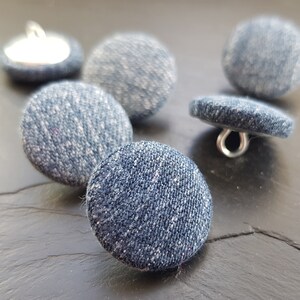 May include: A set of six blue denim buttons with silver metal shanks. The buttons are round and have a textured surface.
