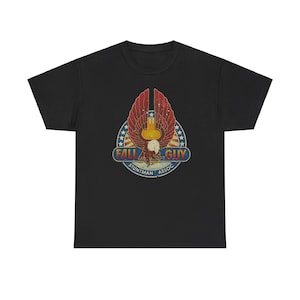 May include: Black t-shirt featuring a distressed graphic. The graphic includes a stylized eagle with red and yellow wings, a blue and white star-studded circle, and the text "FALL GUY STUNTMAN ASSOC."