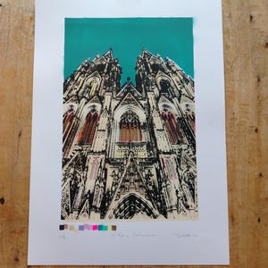 May include: A colorful screen print of a cathedral with a teal blue sky. The print is signed "Cologne Cathedral" and numbered "2/6".