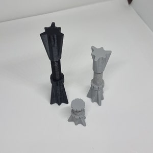 May include: Three 3D-printed objects with a star-shaped top and a threaded shaft. One is black, one is grey, and the smallest is also grey. The objects are standing upright on a white surface.