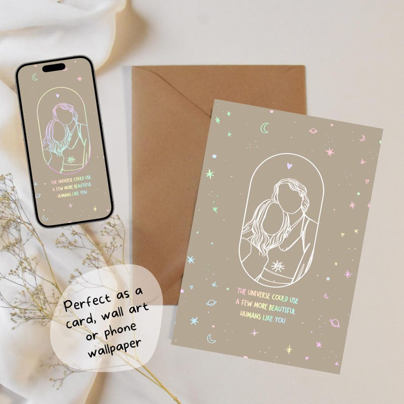 May include: A light brown card with a white outline of a couple standing together. The card has a rainbow gradient of stars, moons, and planets. The text on the card reads "The universe could use a few more beautiful humans like you!"
