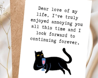 May include: A greeting card with a black cat illustration holding a glass of pink liquid. The card has the text "Dear love of my life, I've truly enjoyed annoying you all this time and I look forward to continuing forever."