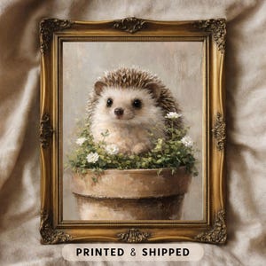 May include: A framed print featuring a charming hedgehog nestled in a terracotta pot filled with greenery and small white flowers. The hedgehog has brown and white quills and a sweet expression. The ornate gold frame adds a vintage touch to the artwork.
