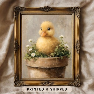 May include: A framed print of a yellow duckling in a brown pot with white flowers and green foliage. The print is in a gold ornate frame. The text "PRINTED & SHIPPED" is at the bottom of the image.